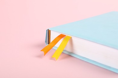 Photo of Book with ribbon bookmarks on pink background, closeup. Space for text