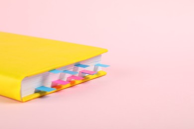 Photo of Book with colorful tabs on pink background, closeup. Space for text