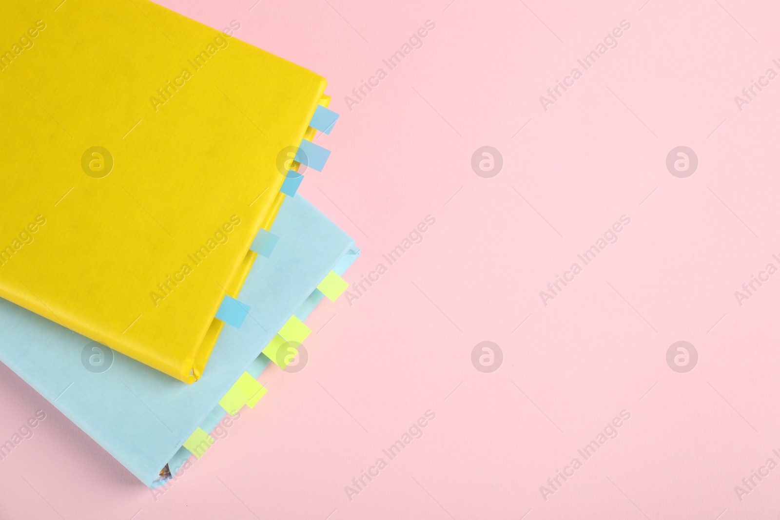 Photo of Books with colorful tabs on pink background, top view. Space for text