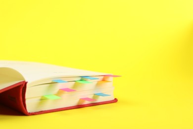 Photo of Book with colorful tabs on yellow background, closeup. Space for text