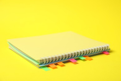 Photo of Notebook with colorful tabs on yellow background, closeup