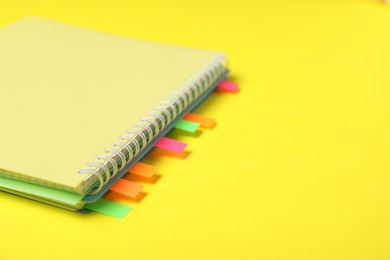 Photo of Notebook with colorful tabs on yellow background, closeup. Space for text