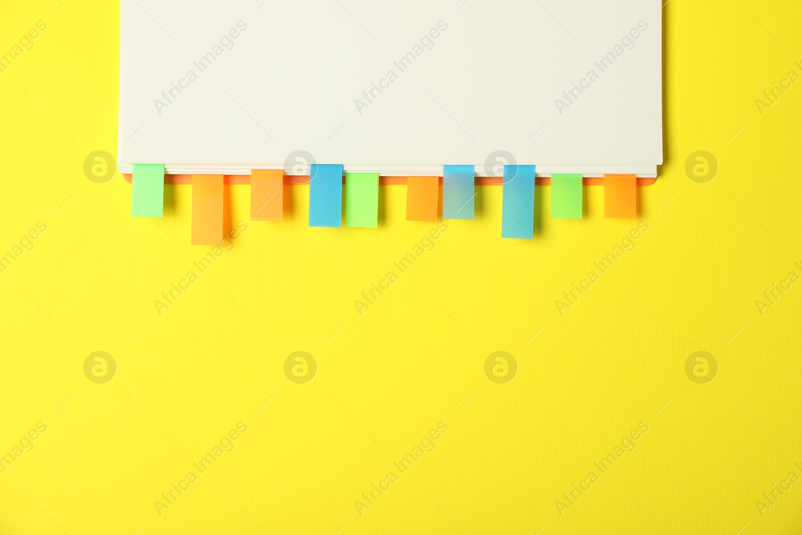 Photo of Notebook with colorful tabs on yellow background, top view. Space for text