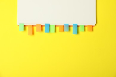 Photo of Notebook with colorful tabs on yellow background, top view. Space for text