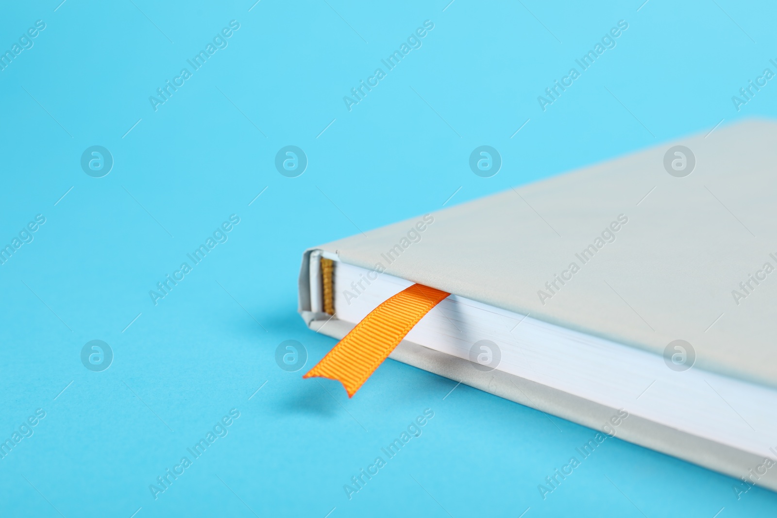 Photo of Book with ribbon bookmark on light blue background, closeup. Space for text