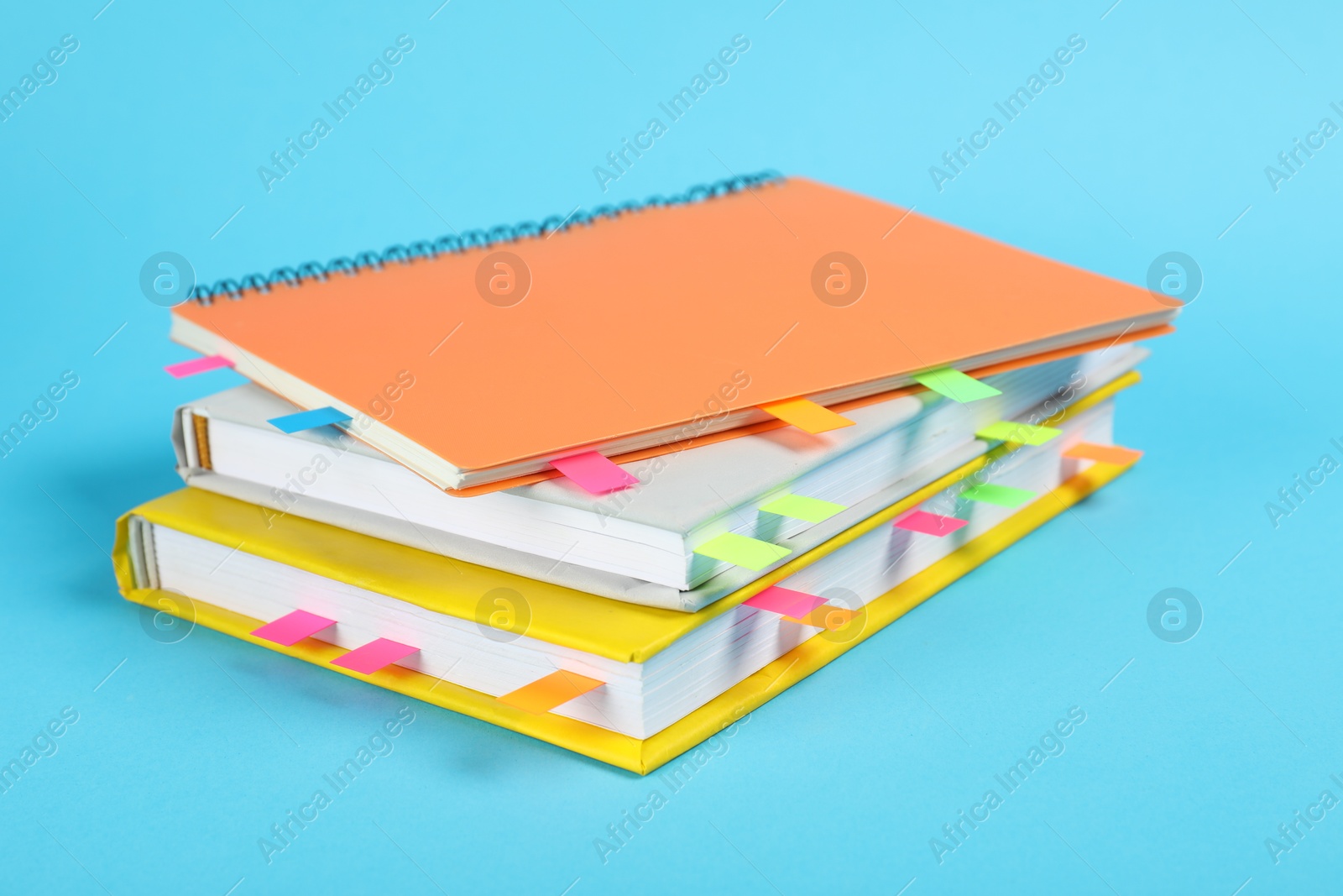 Photo of Books and notebook with colorful tabs on light blue background, closeup