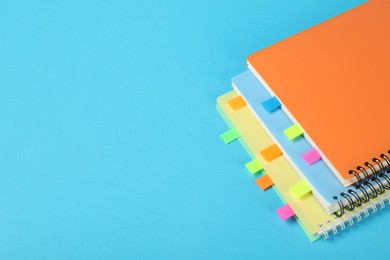 Photo of Notebooks with colorful tabs on light blue background, closeup. Space for text