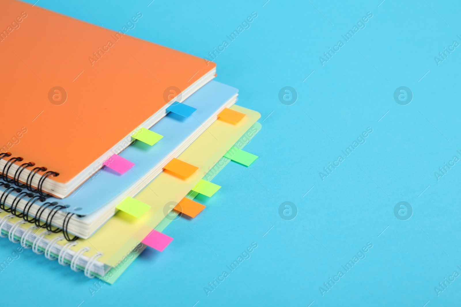 Photo of Notebooks with colorful tabs on light blue background, closeup. Space for text