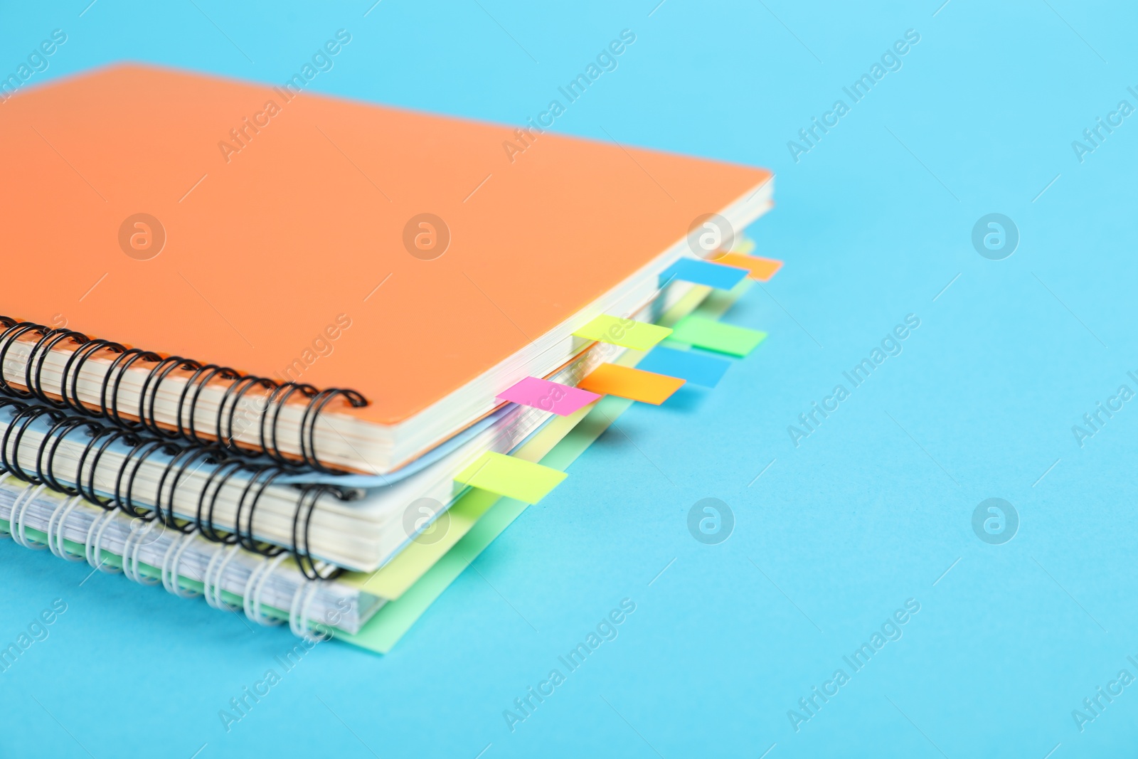 Photo of Notebooks with colorful tabs on light blue background, closeup. Space for text