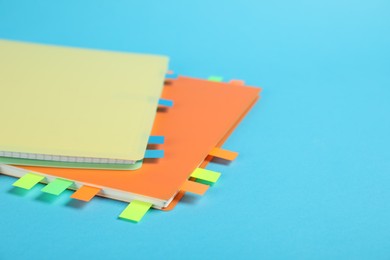 Photo of Notebooks with colorful tabs on light blue background, closeup. Space for text