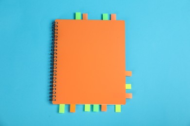 Photo of Notebook with colorful tabs on light blue background, top view