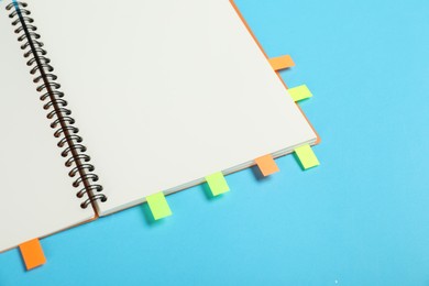 Photo of Notebook with colorful tabs on light blue background, closeup