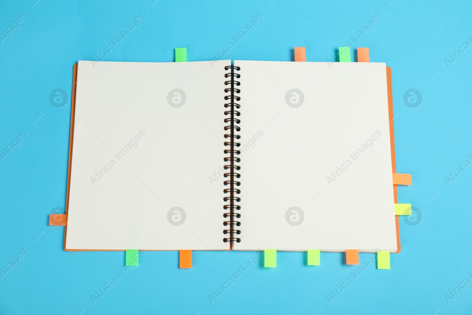 Photo of Notebook with colorful tabs on light blue background, top view