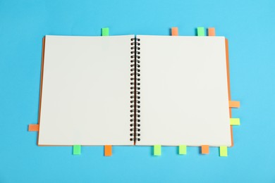 Photo of Notebook with colorful tabs on light blue background, top view