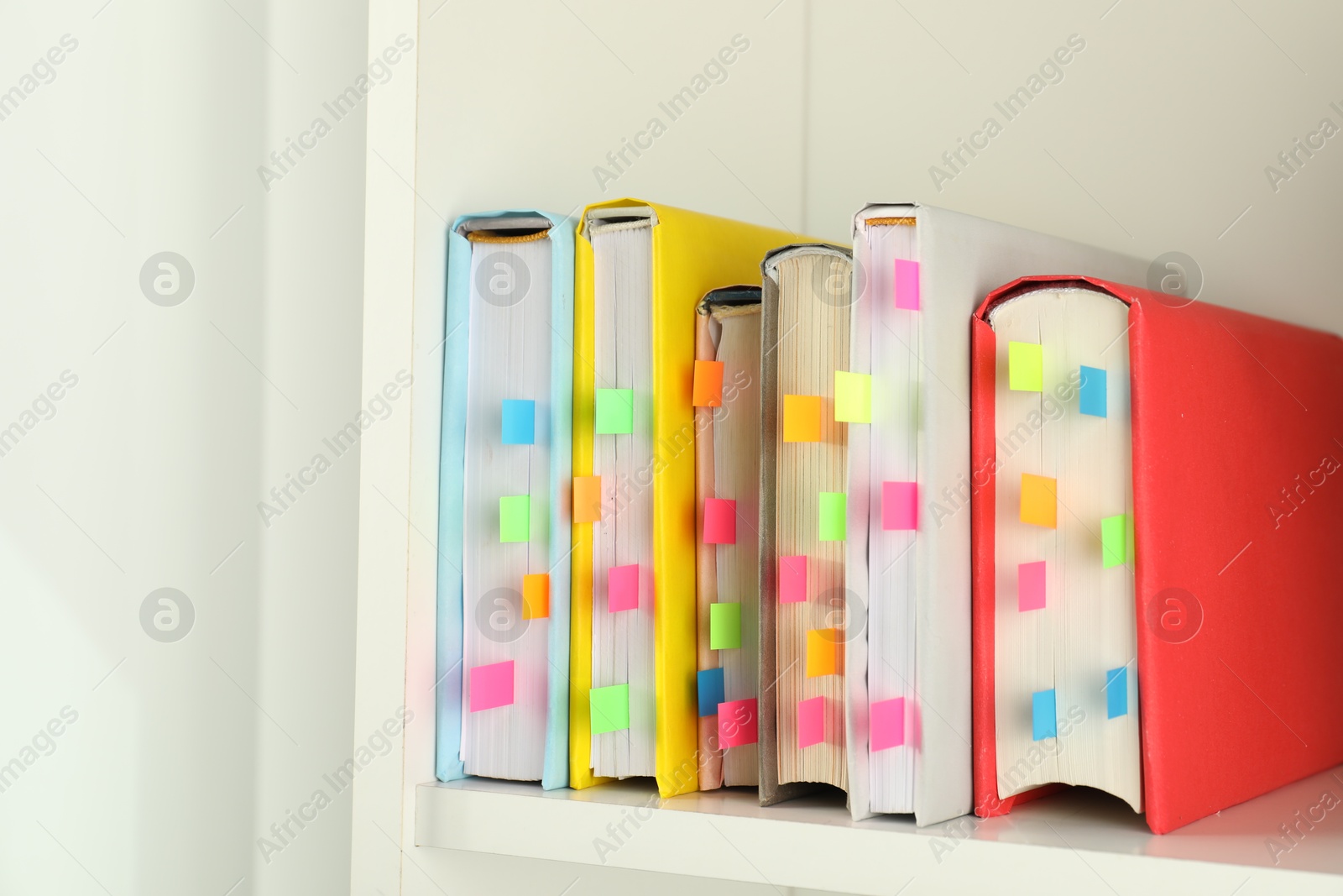 Photo of Books with colorful tabs on white shelf indoors