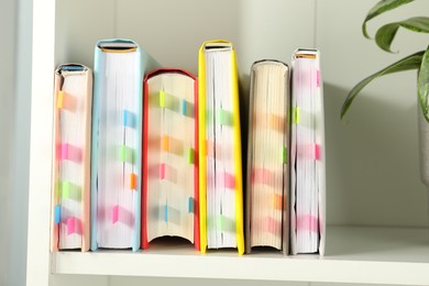 Photo of Books with colorful tabs on white shelf indoors