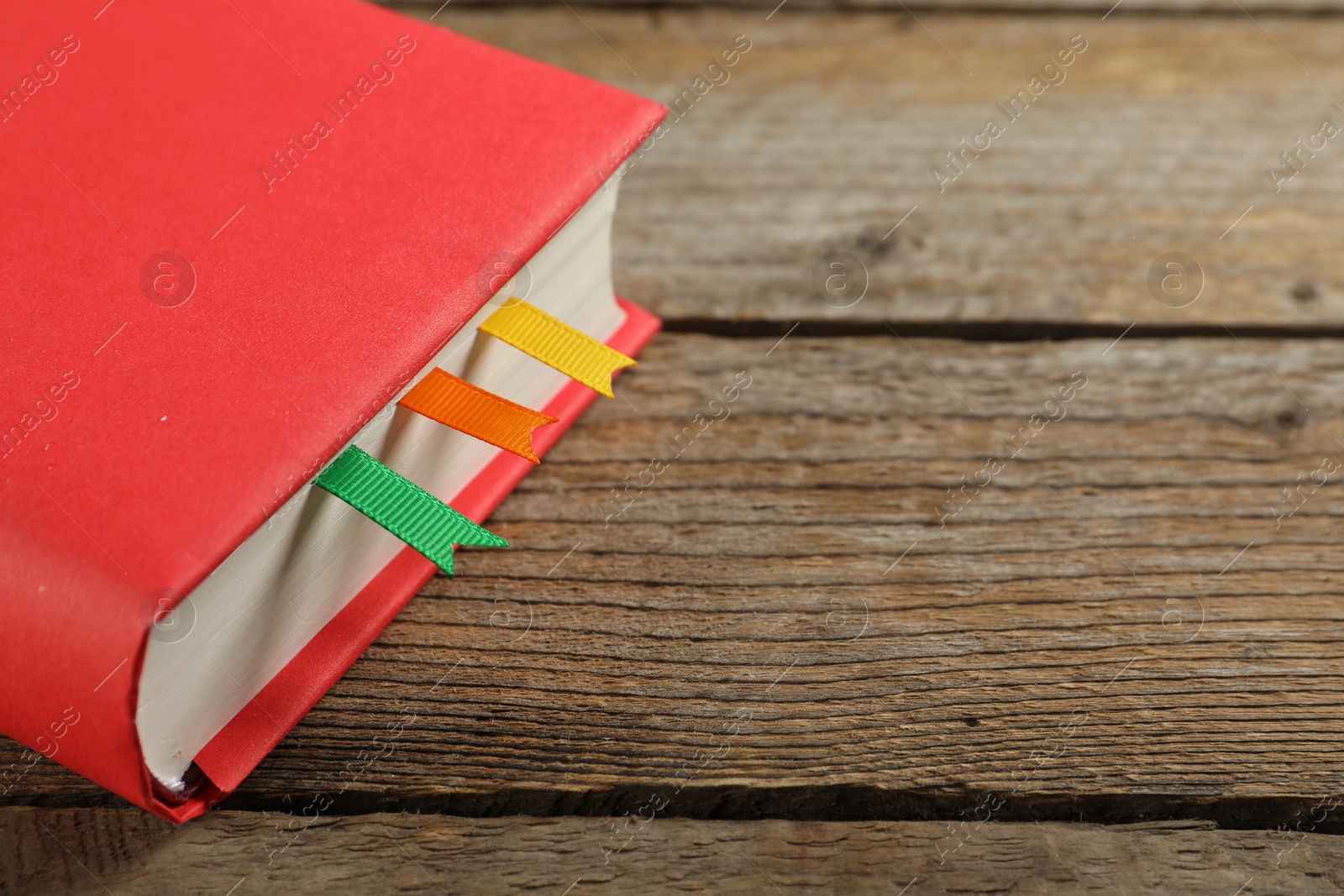 Photo of Book with ribbon bookmarks on wooden table, closeup. Space for text