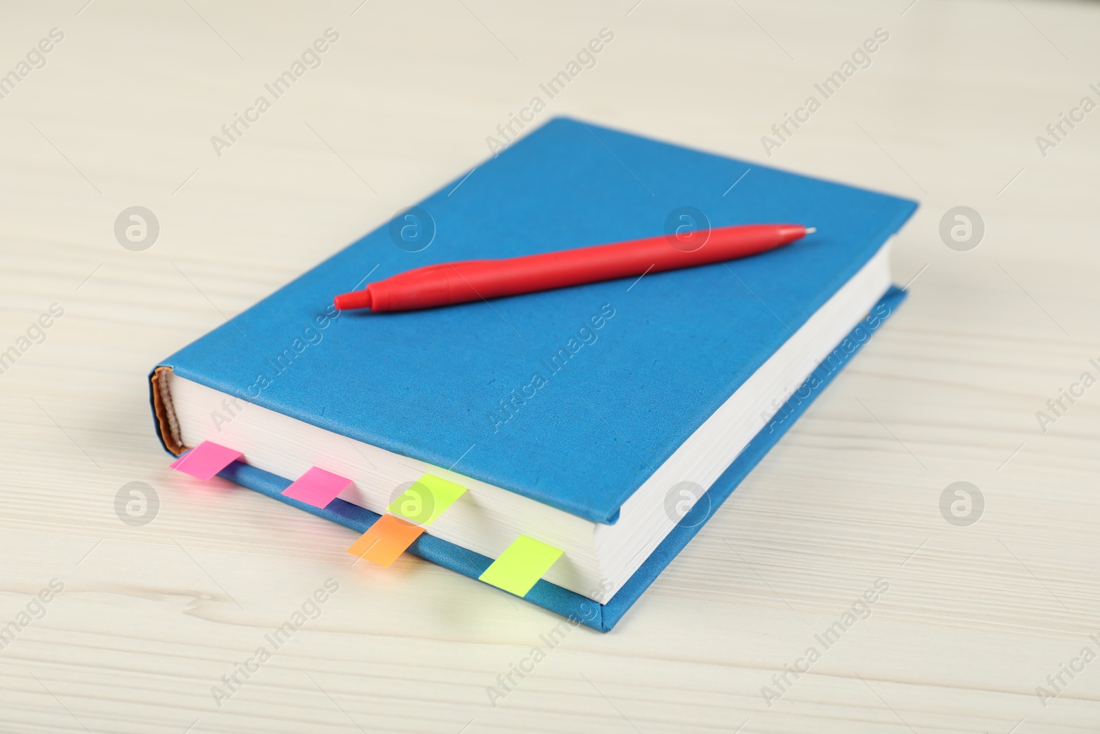 Photo of Book with colorful tabs and pen on light wooden table, closeup