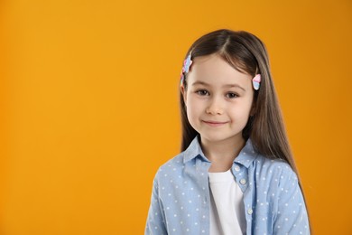 Photo of Smiling little girl wearing beautiful hair accessories on orange background, space for text