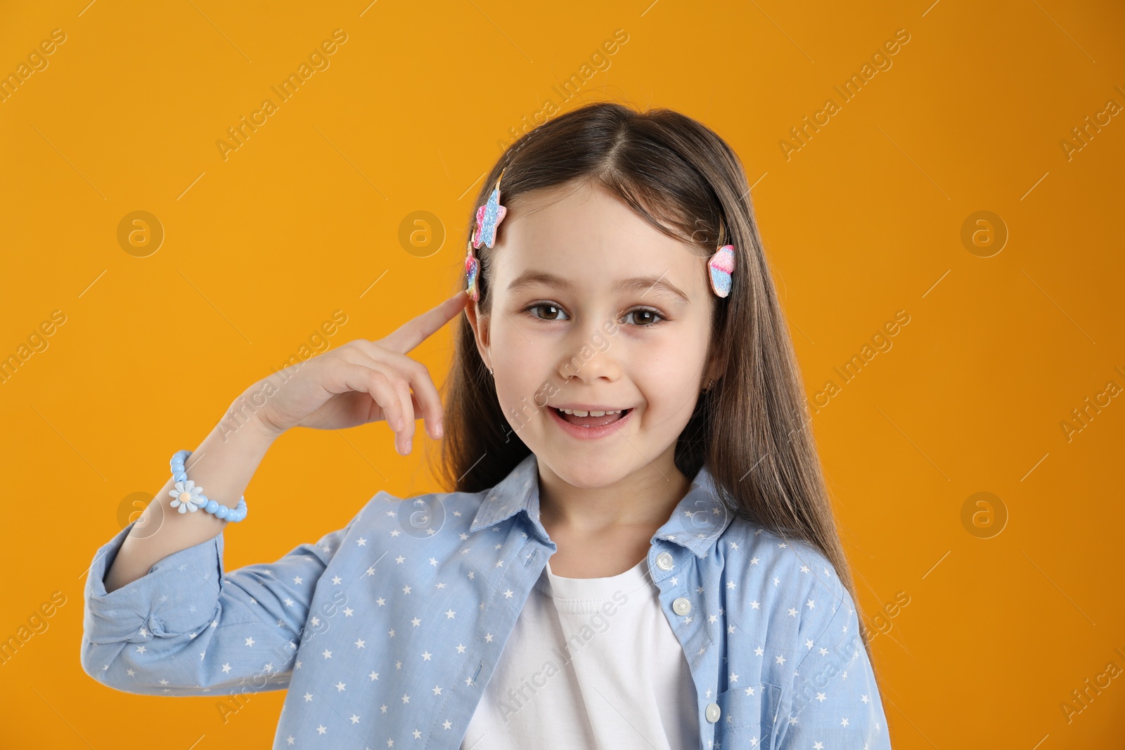 Photo of Happy little girl wearing beautiful hair accessories on orange background