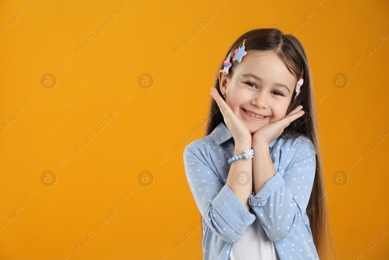 Photo of Happy little girl wearing beautiful hair accessories on orange background, space for text