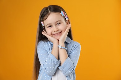 Photo of Happy little girl wearing beautiful hair accessories on orange background