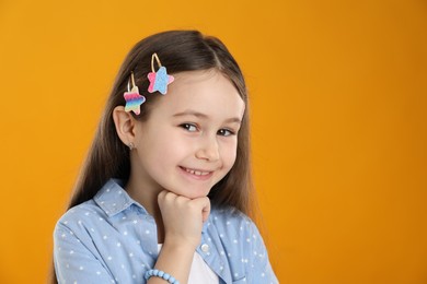 Photo of Happy little girl wearing beautiful hair accessories on orange background, space for text