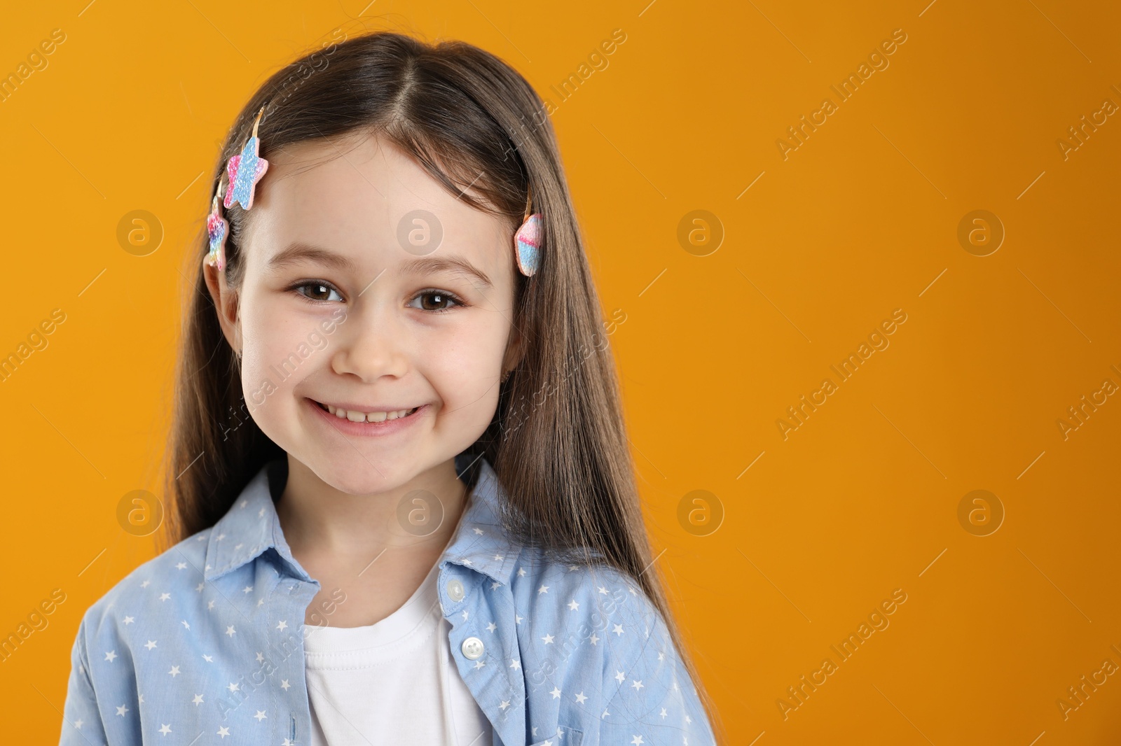 Photo of Happy little girl wearing beautiful hair accessories on orange background, space for text