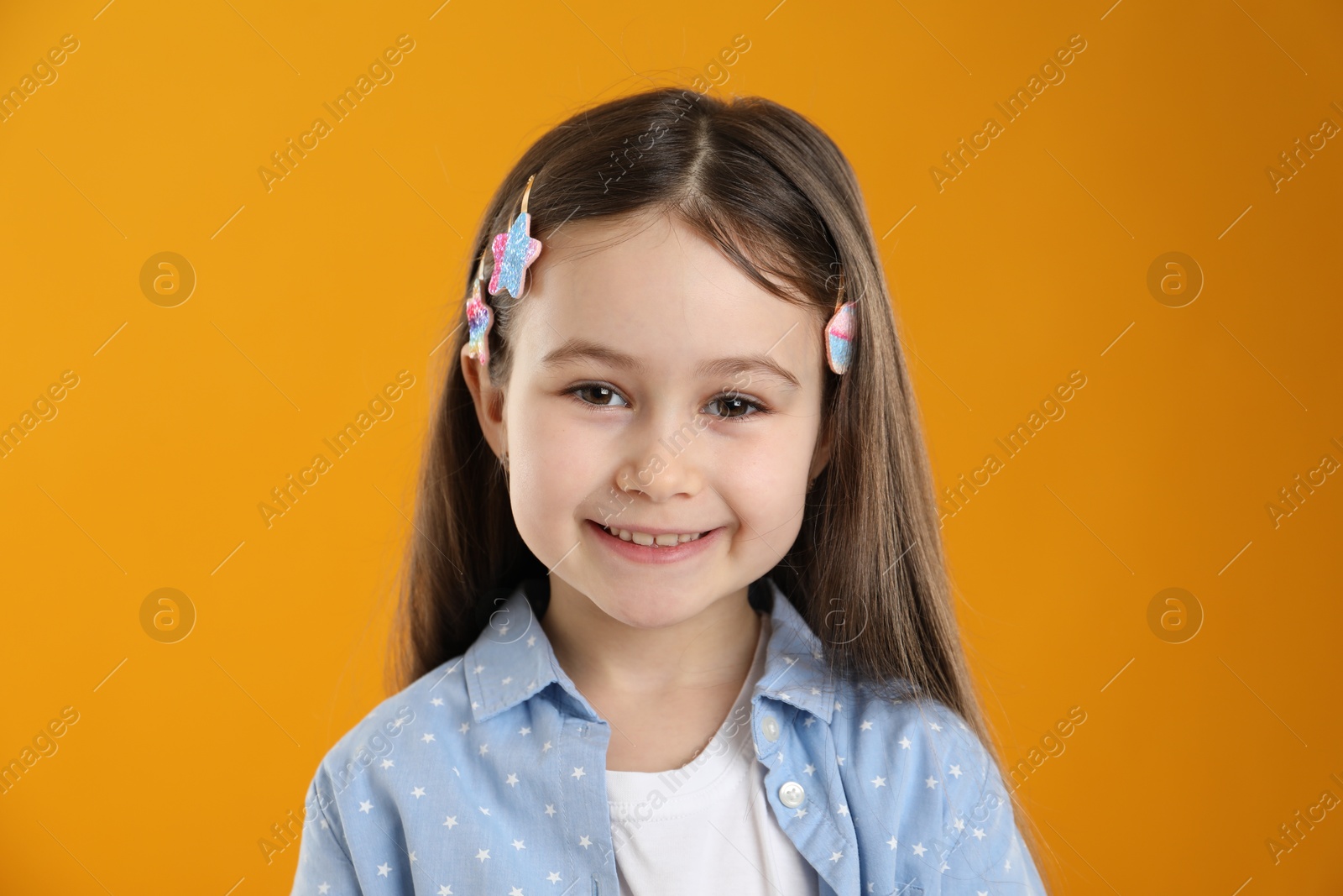 Photo of Happy little girl wearing beautiful hair accessories on orange background