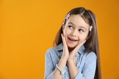 Photo of Happy little girl wearing beautiful hair accessories on orange background, space for text