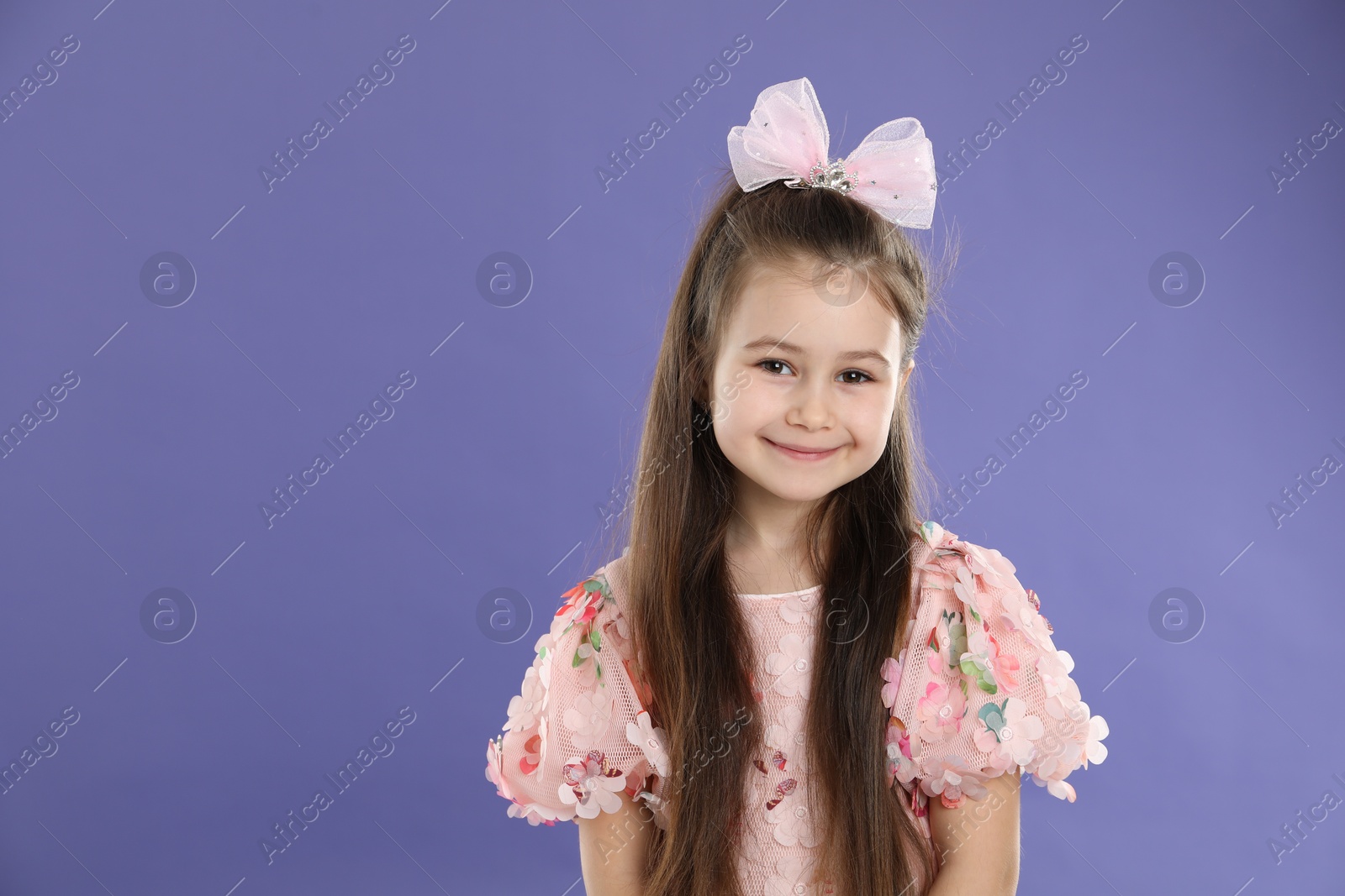 Photo of Happy little girl wearing beautiful hair accessory on purple background, space for text