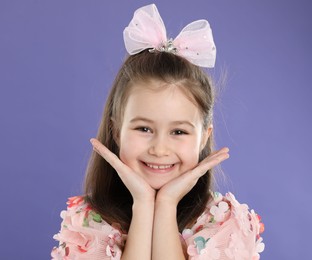 Photo of Happy little girl wearing beautiful hair accessory on purple background