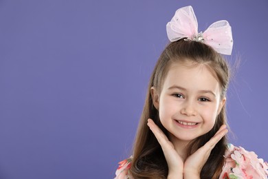 Photo of Happy little girl wearing beautiful hair accessory on purple background, space for text