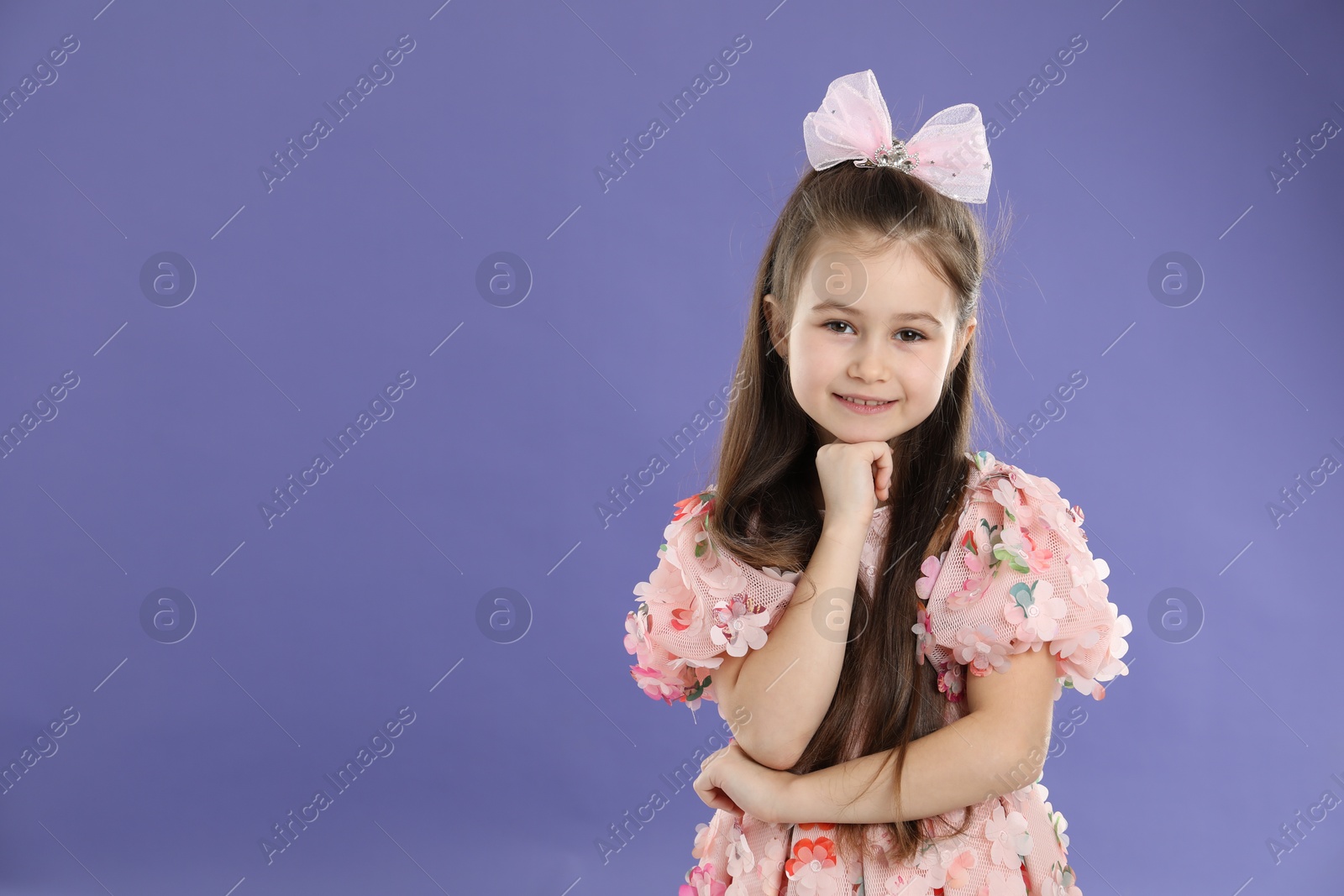 Photo of Happy little girl wearing beautiful hair accessory on purple background, space for text