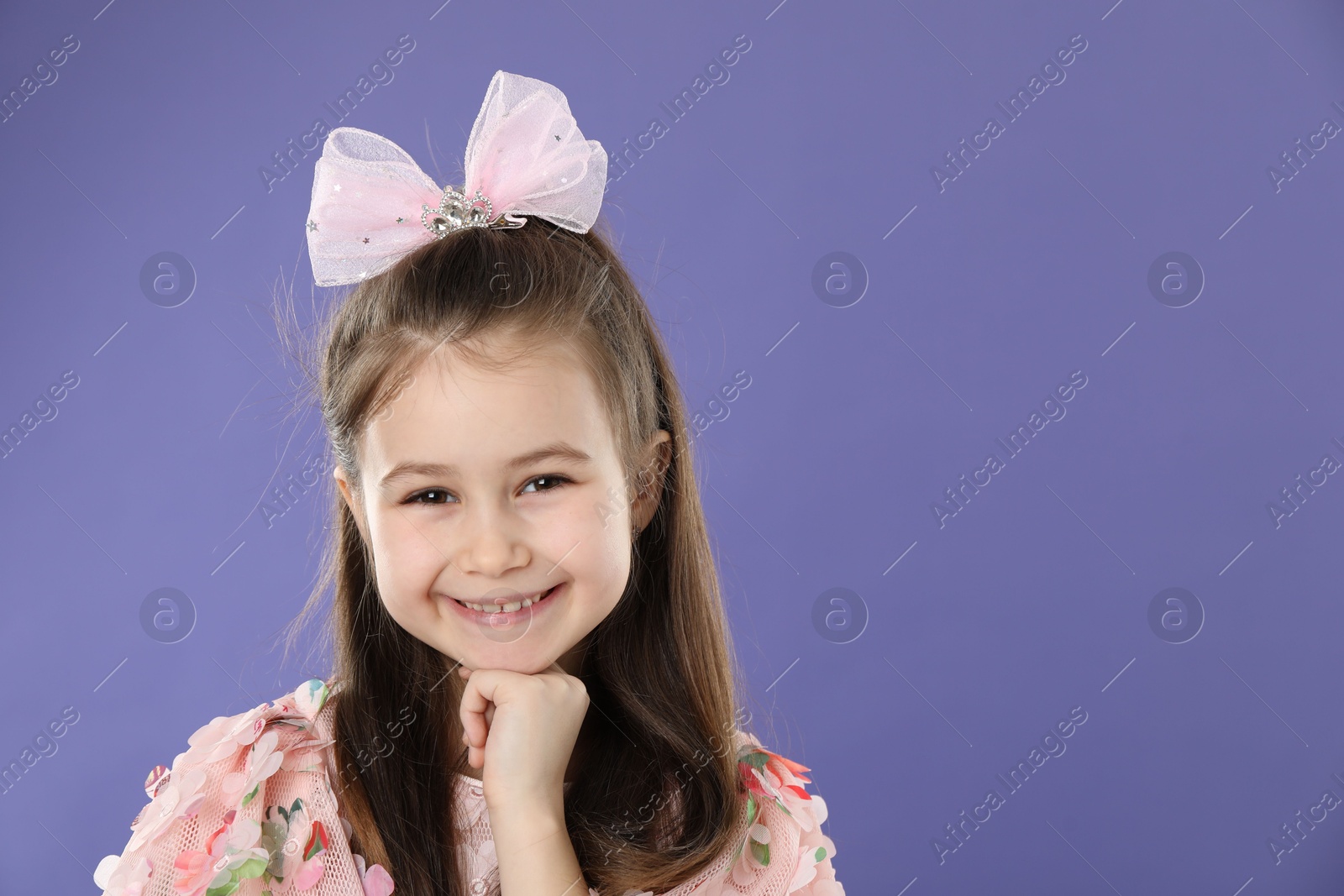 Photo of Happy little girl wearing beautiful hair accessory on purple background, space for text