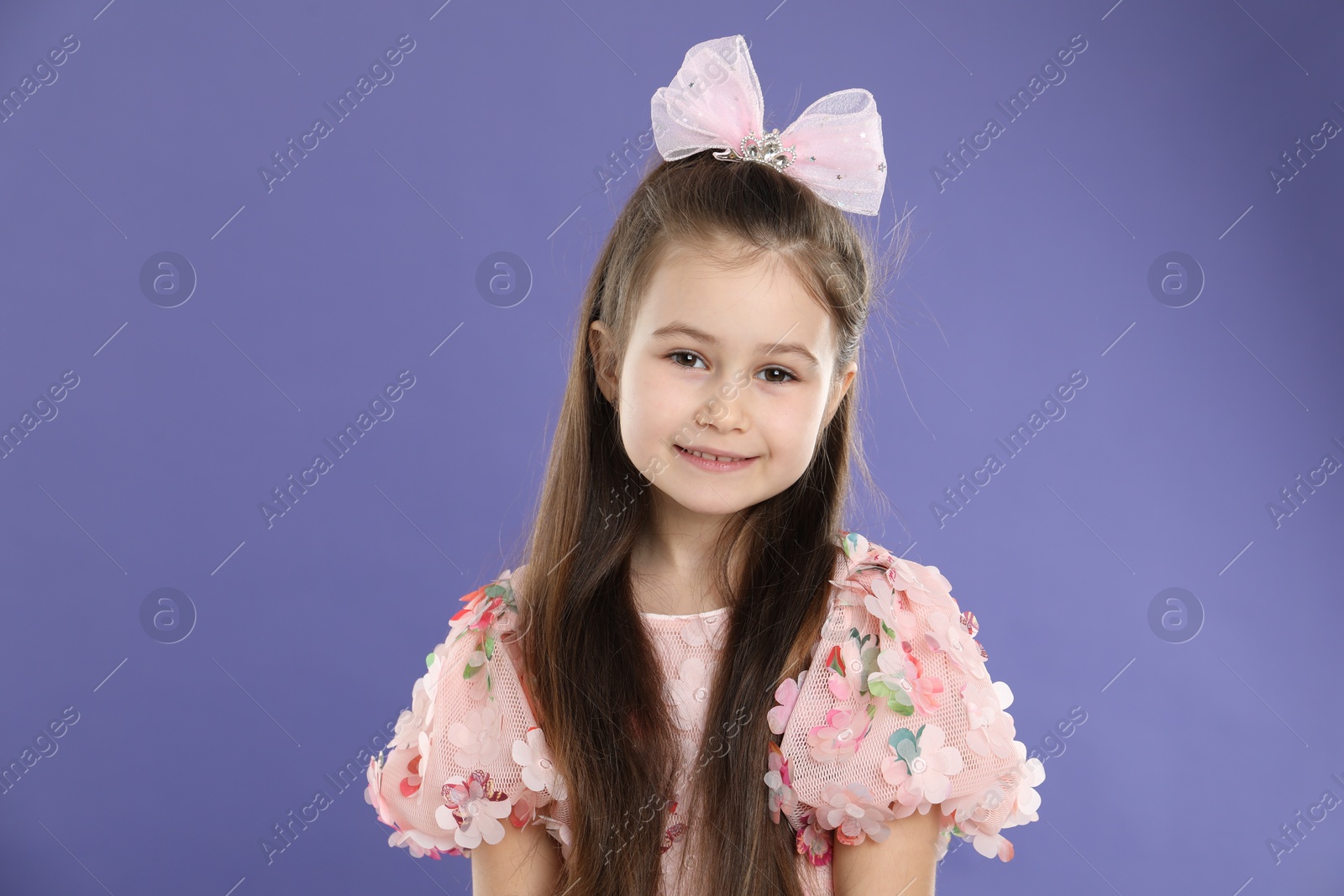 Photo of Happy little girl wearing beautiful hair accessory on purple background