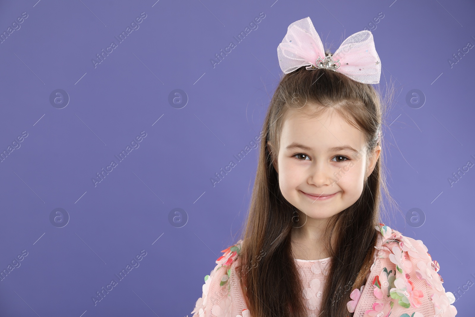 Photo of Happy little girl wearing beautiful hair accessory on purple background, space for text