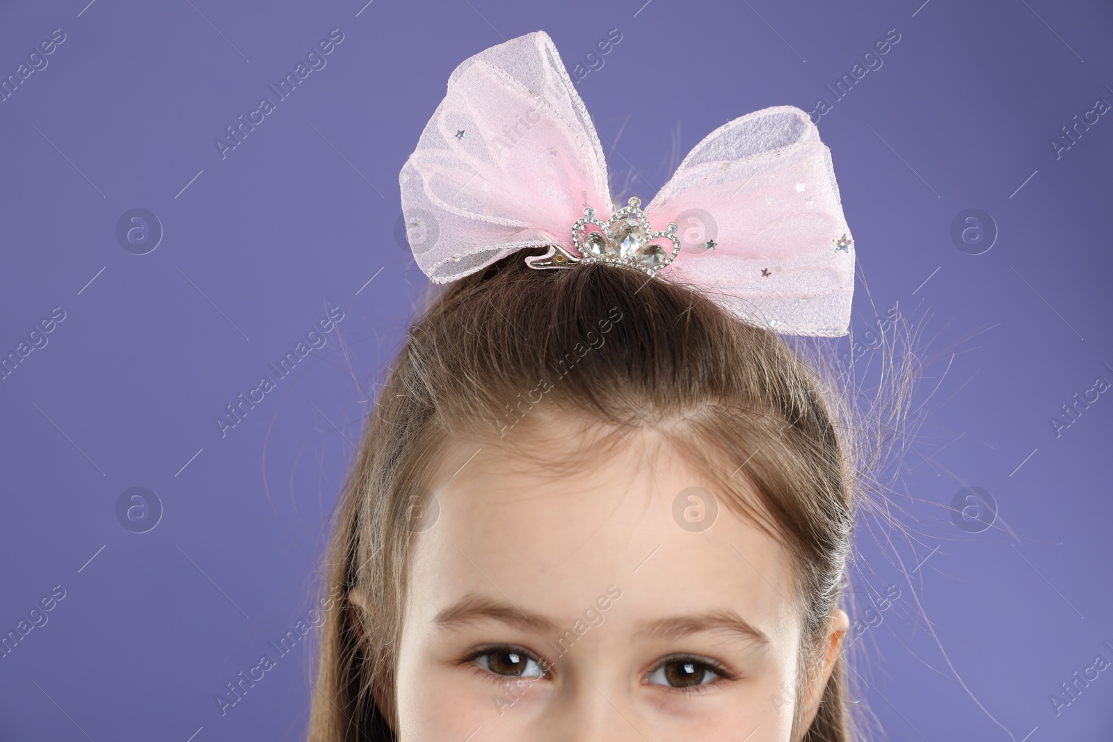 Photo of Little girl wearing beautiful hair accessory on purple background, closeup