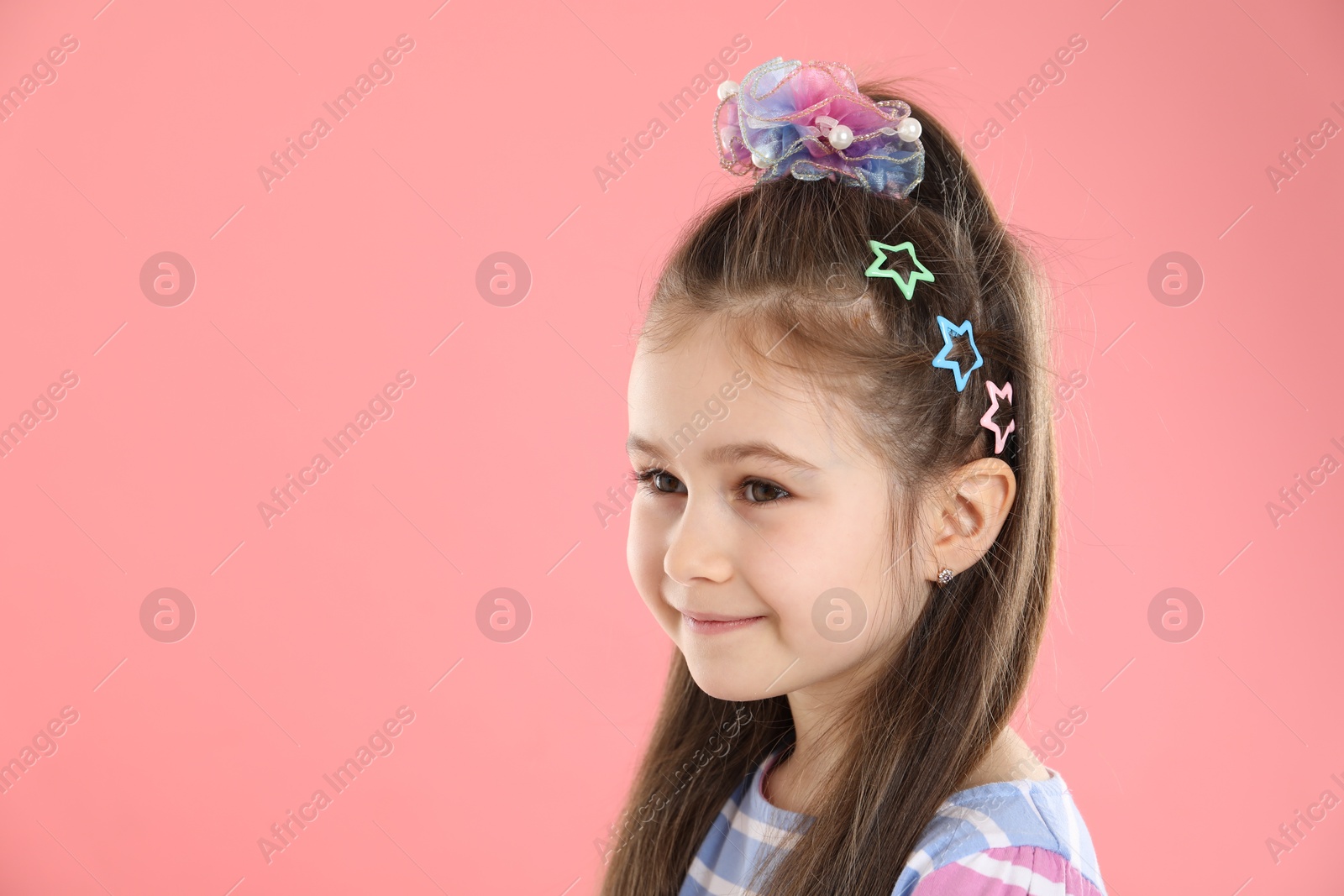 Photo of Happy little girl wearing beautiful hair accessories on pink background, space for text