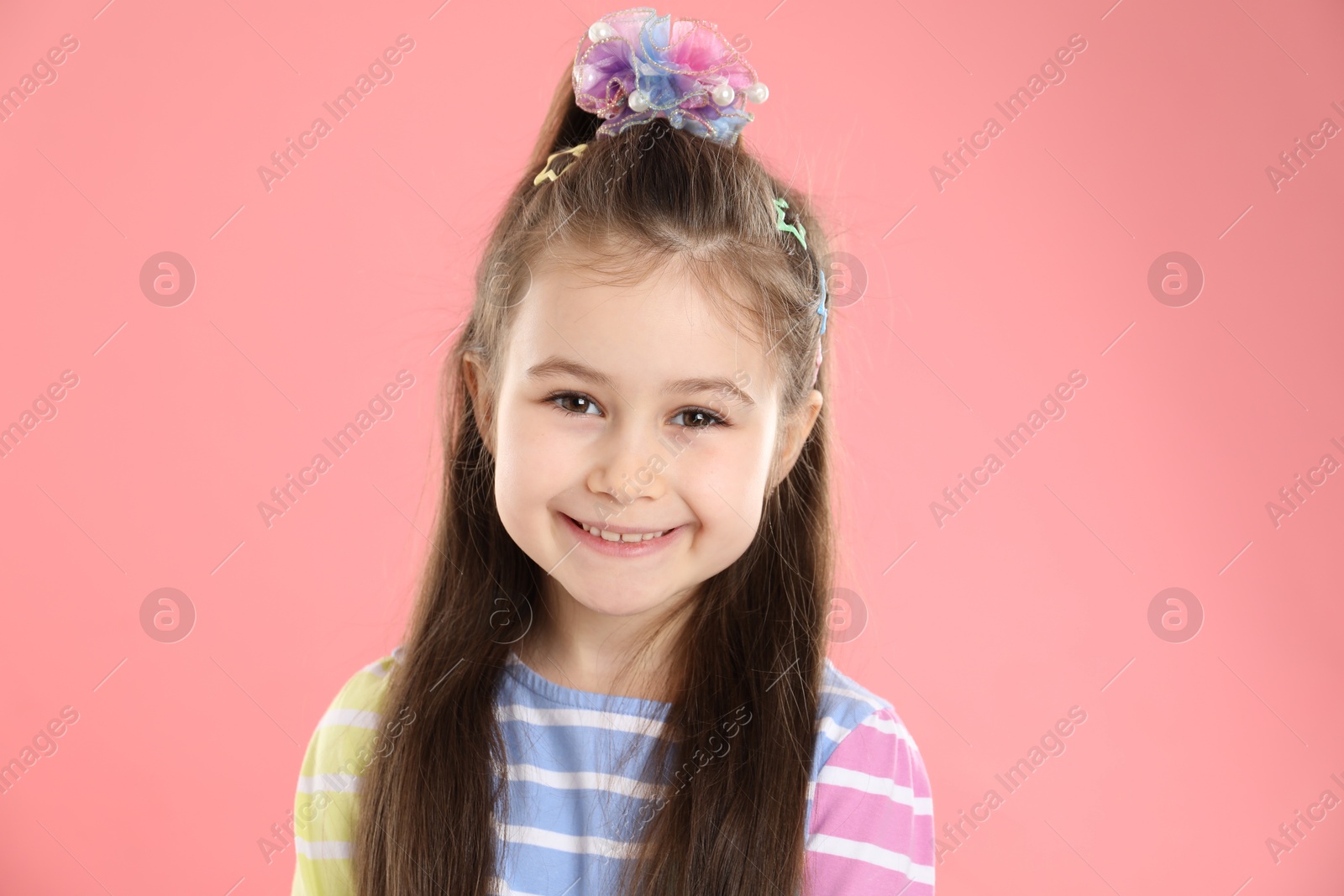 Photo of Happy little girl wearing beautiful hair accessories on pink background