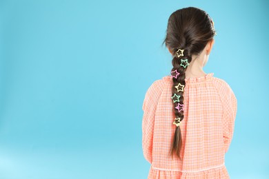 Photo of Little girl wearing beautiful hair accessories on light blue background, back view. Space for text