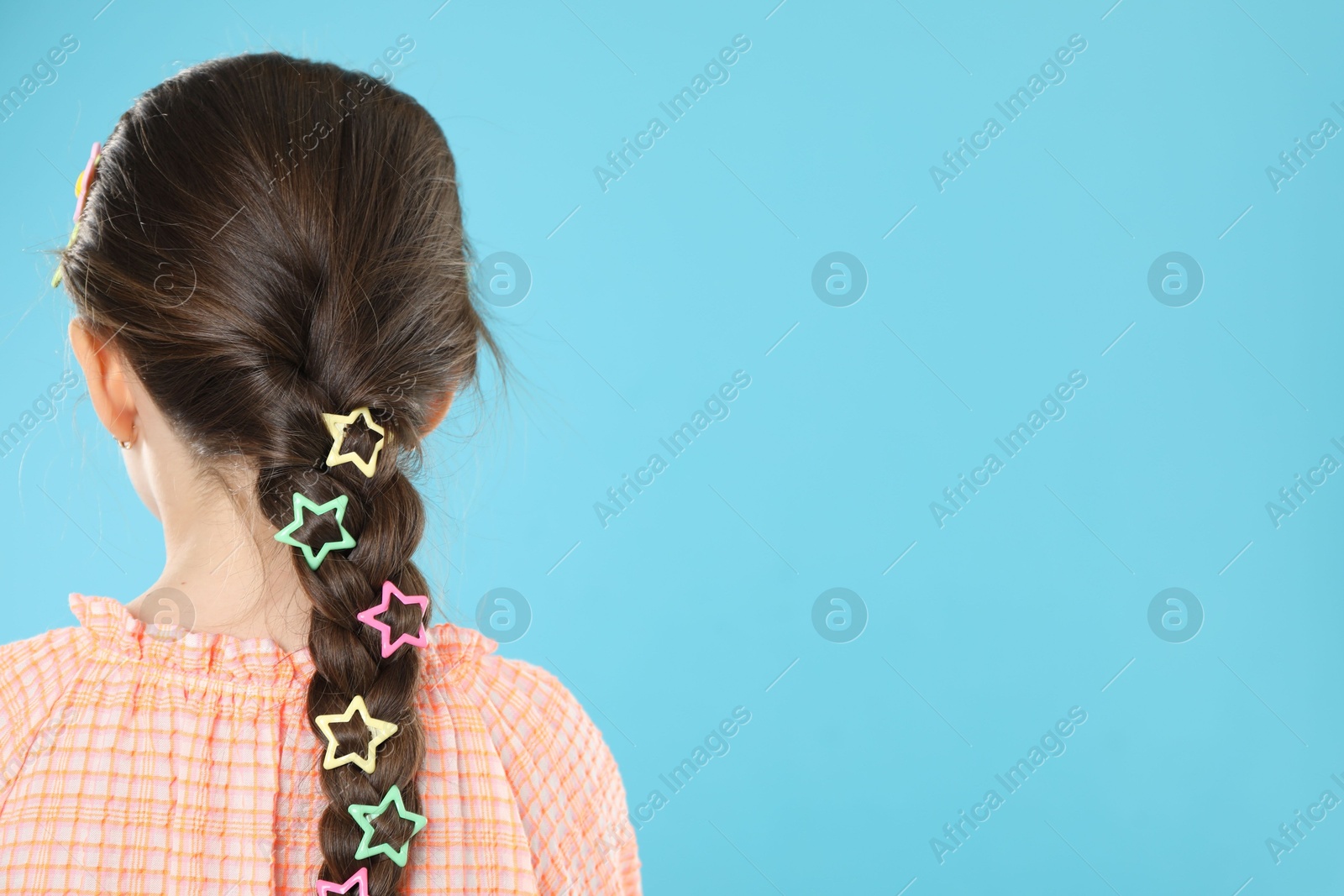 Photo of Little girl wearing beautiful hair accessories on light blue background, back view. Space for text