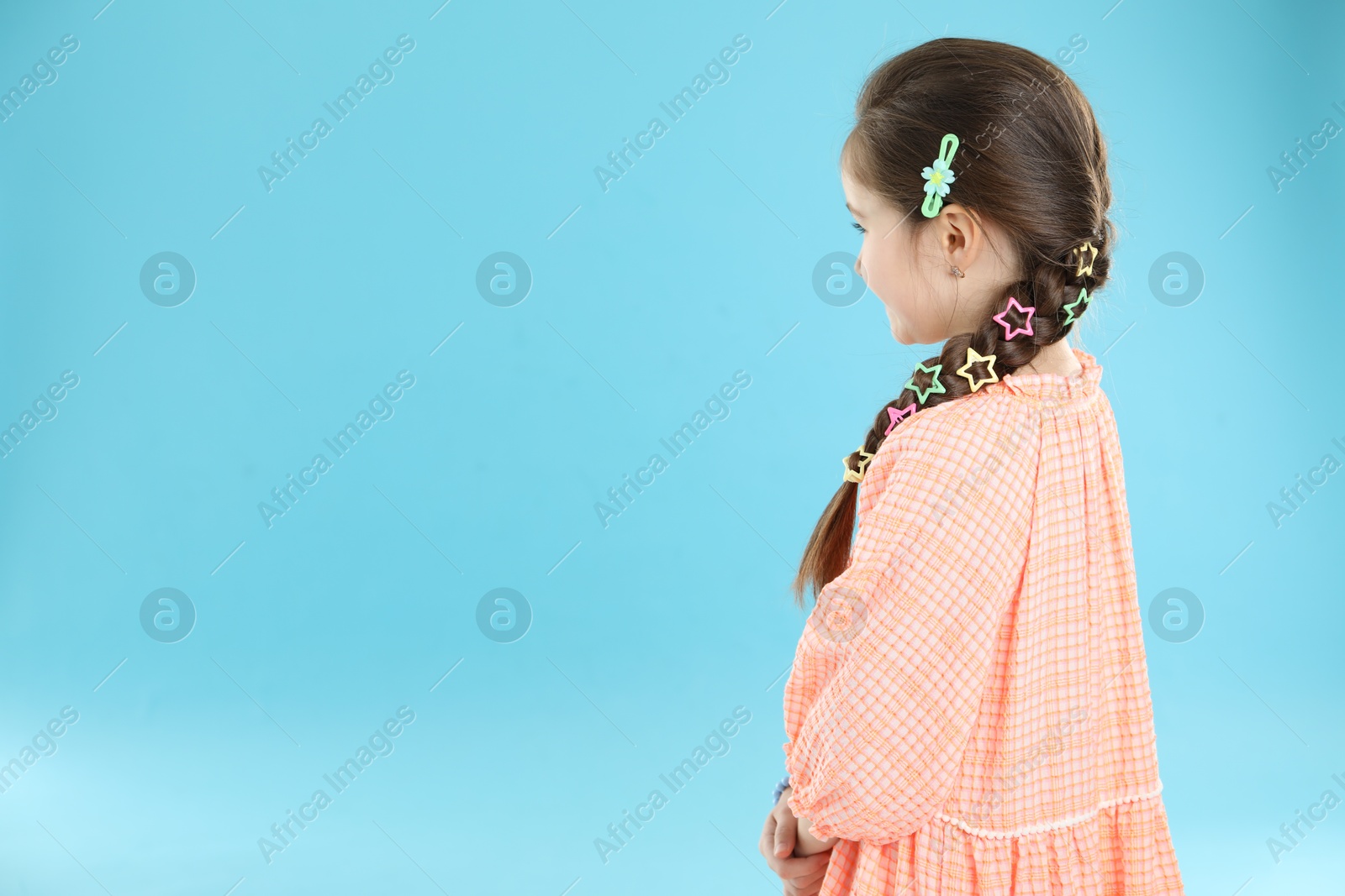 Photo of Little girl wearing beautiful hair accessories on light blue background, space for text