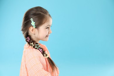 Photo of Little girl wearing beautiful hair accessories on light blue background, space for text