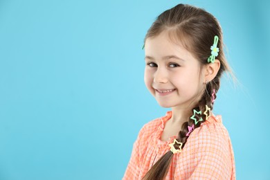 Photo of Little girl wearing beautiful hair accessories on light blue background, space for text