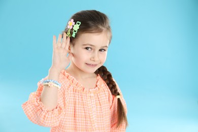 Photo of Little girl wearing beautiful hair accessories on light blue background, space for text