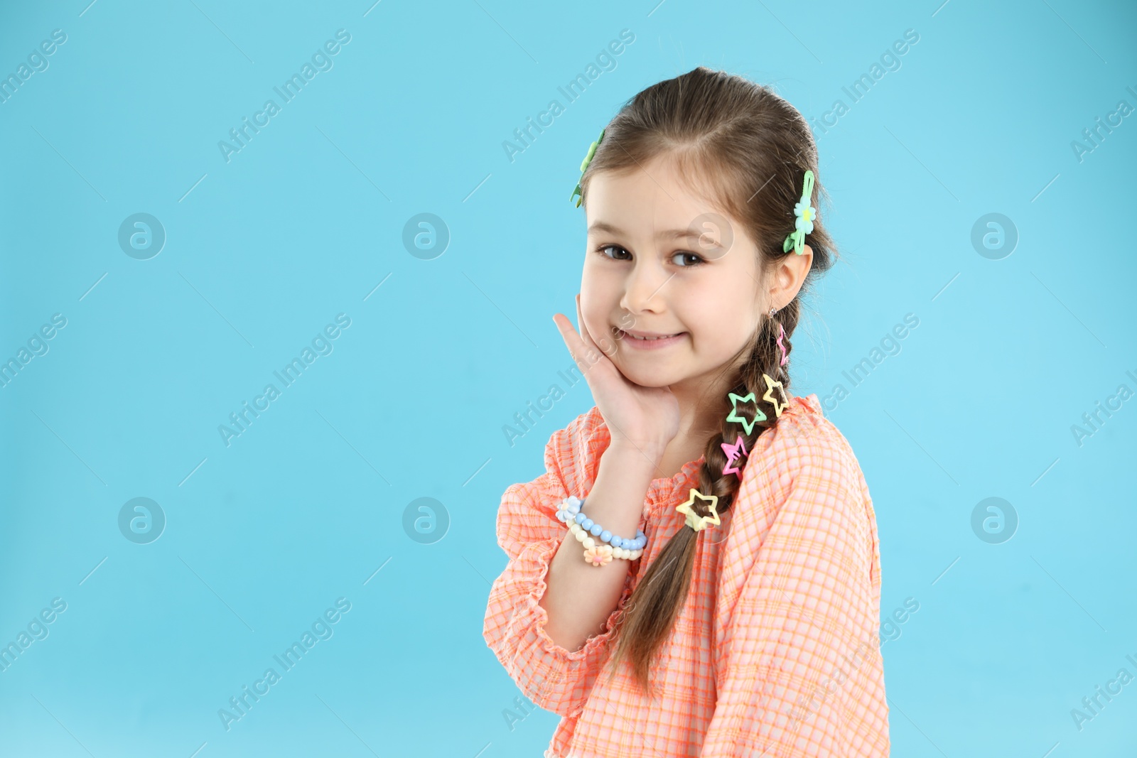 Photo of Little girl wearing beautiful hair accessories on light blue background, space for text