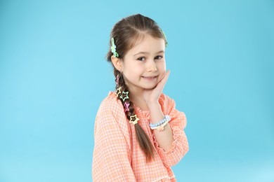 Photo of Little girl wearing beautiful hair accessories on light blue background