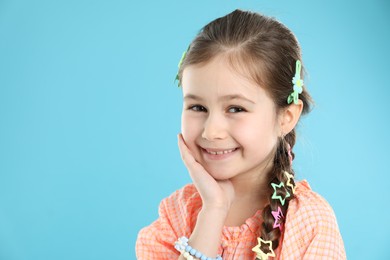 Photo of Little girl wearing beautiful hair accessories on light blue background, space for text