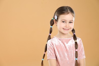 Photo of Little girl wearing beautiful hair accessories on beige background, space for text